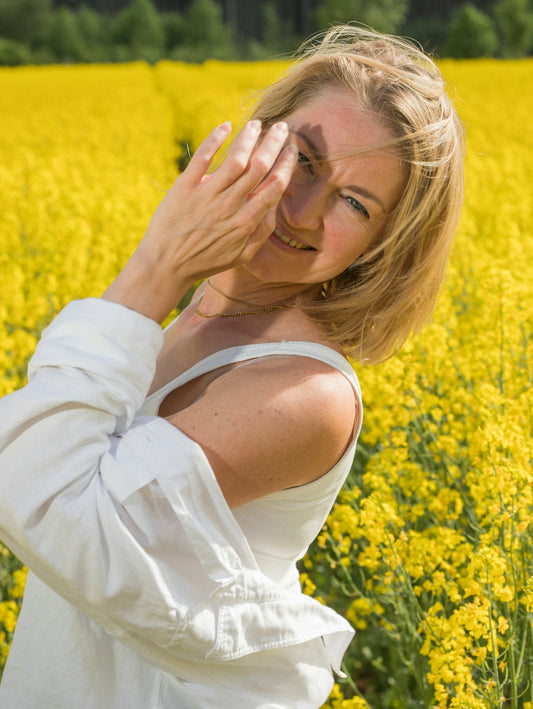 Woman shielding her face in a field of yellow flowers.